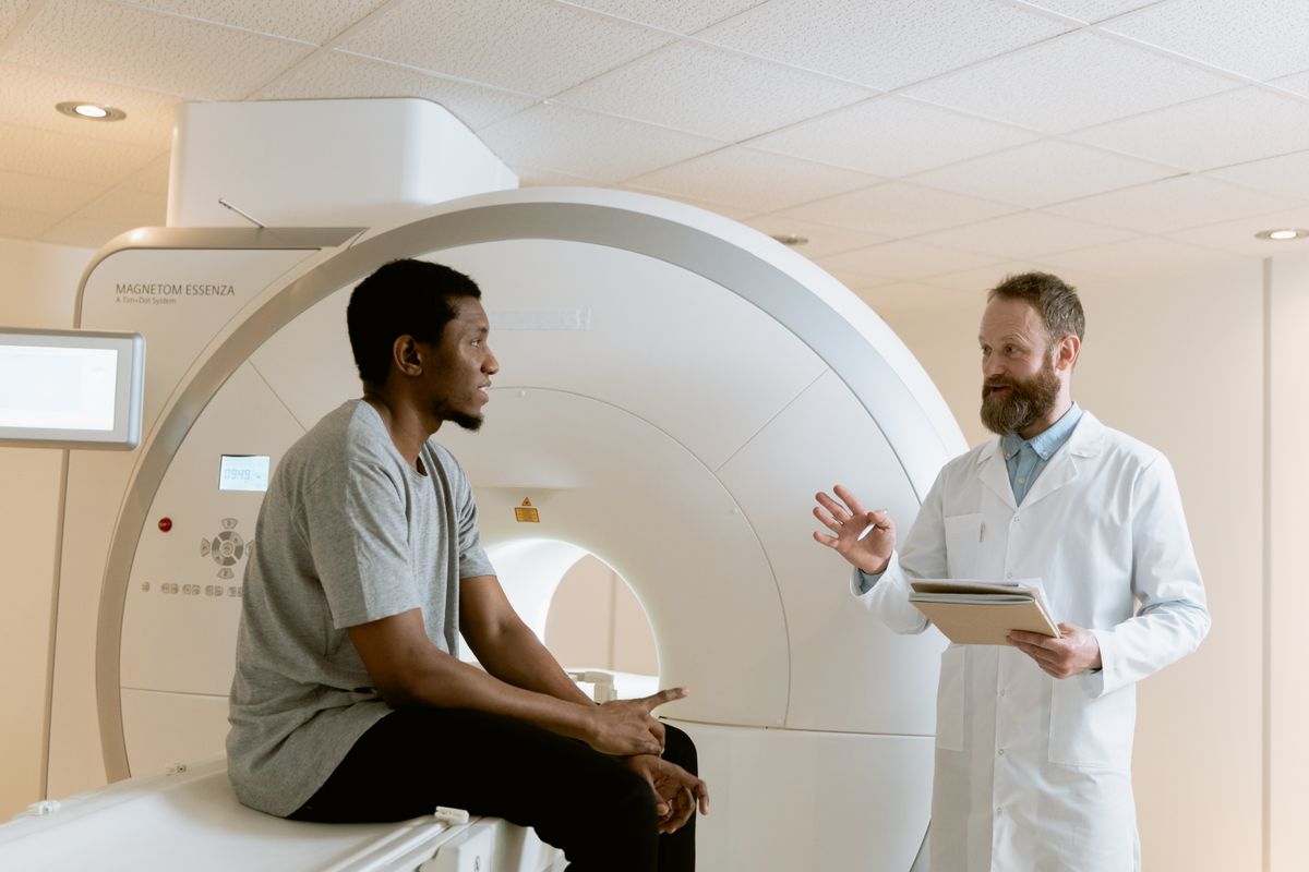 An imaging professional holding a clipboard, talking with a patient seated on an MRI table